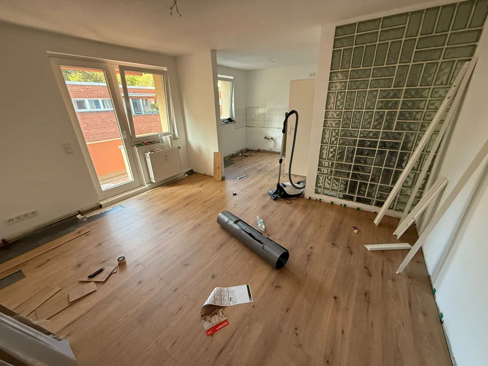 Derselbe Wohnraum mit neuem Laminat in Holzoptik während der Verlegung